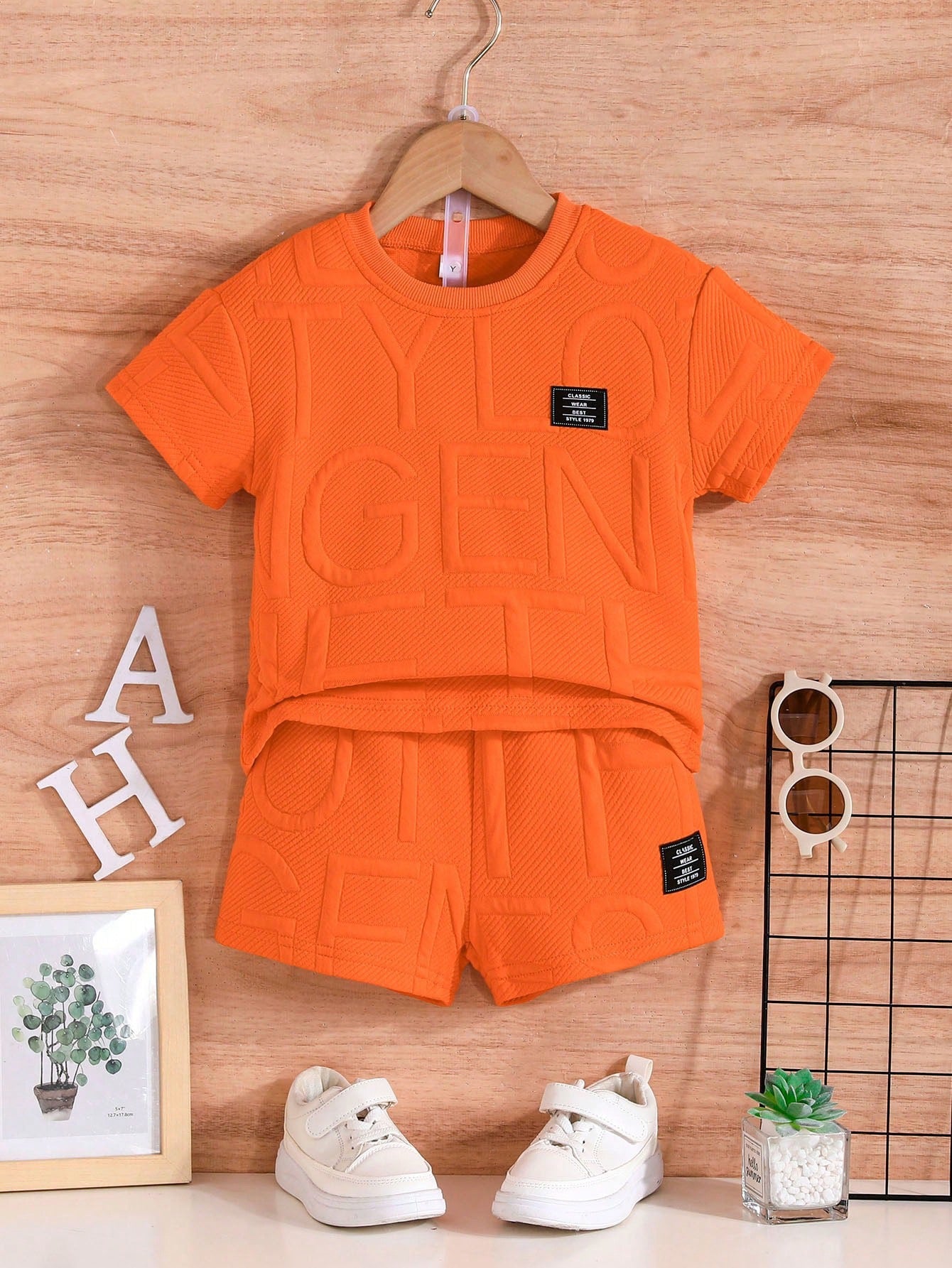 Un ensemble d'été orange de la marque AURORE LUXURE, disposé sur un cintre avec des chaussures blanches. Idéal pour les enfants de 4 à 7 ans. Ensemble de vêtements d'été pour jeunes garçons.