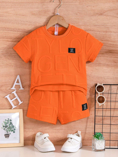 Un ensemble d'été orange de la marque AURORE LUXURE, disposé sur un cintre avec des chaussures blanches. Idéal pour les enfants de 4 à 7 ans. Ensemble de vêtements d'été pour jeunes garçons.
